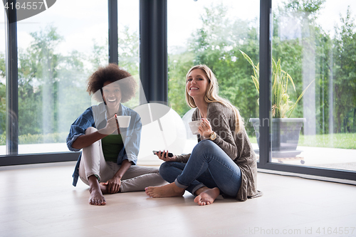 Image of multiethnic women sit on the floor and drinking coffee