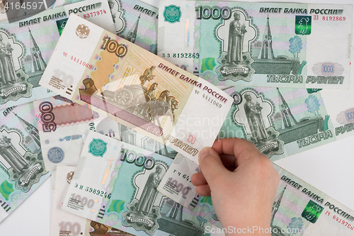 Image of Children\'s hand takes the denomination from the pile of randomly scattered Russian banknotes of different denomination