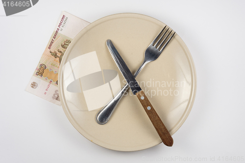 Image of Empty plate with fork and knife, close is a hundred-ruble note, white background