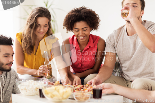 Image of happy friends with drinks eating pizza at home