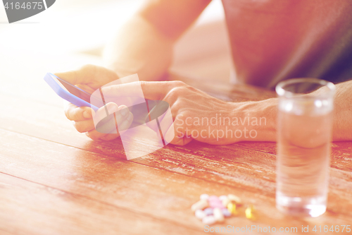 Image of close up of hands with smartphone, pills and water