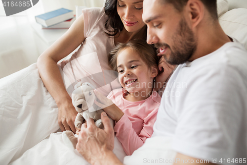 Image of happy child with toy and parents in bed at home