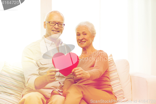 Image of happy senior couple with red heart shape at home