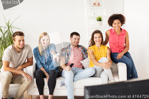 Image of happy friends with remote watching tv at home