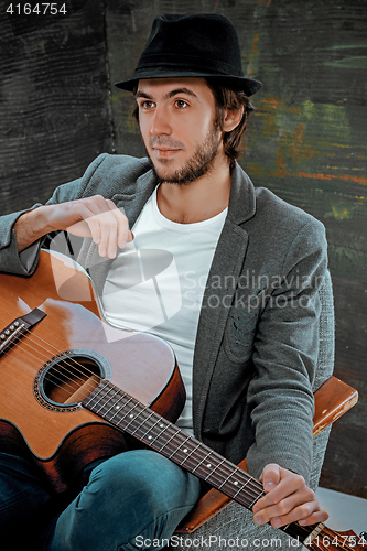 Image of Cool guy sitting with guitar on gray background