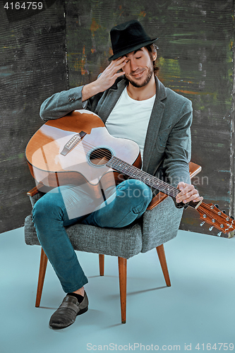 Image of Cool guy sitting with guitar on gray background