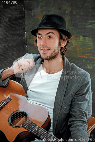 Image of Cool guy sitting with guitar on gray background