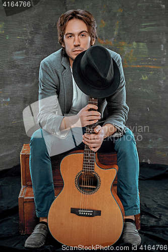 Image of Cool guy sitting with guitar on gray background