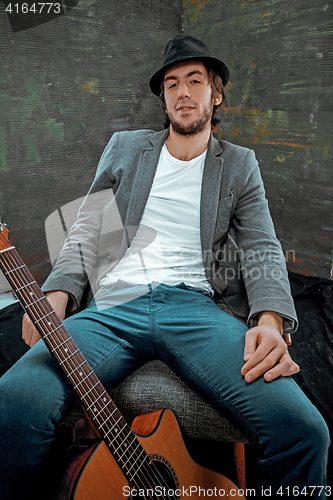 Image of Cool guy sitting with guitar on gray background