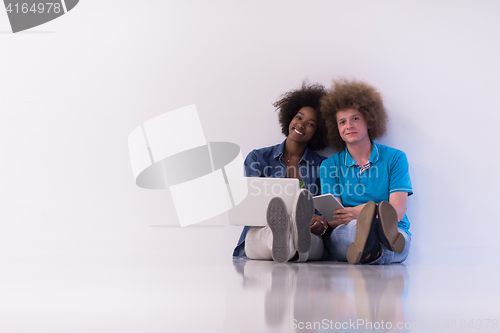Image of multiethnic couple sitting on the floor with a laptop and tablet