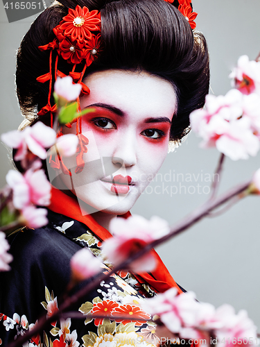 Image of young pretty geisha in black kimono among sakura, asian ethno close up