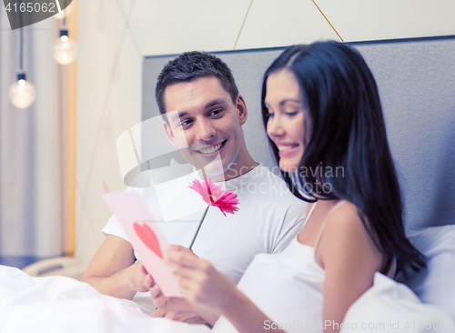 Image of smiling couple in bed with postcard and flower