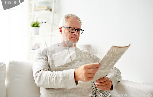 Image of senior man in glasses reading newspaper at home