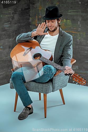 Image of Cool guy sitting with guitar on gray background