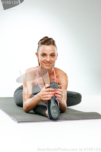 Image of Beautiful slim brunette doing some stretching exercises in a gym