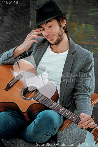 Image of Cool guy sitting with guitar on gray background