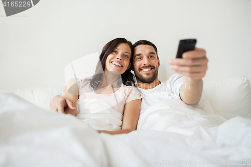 Image of happy couple lying in bed at home and watching tv