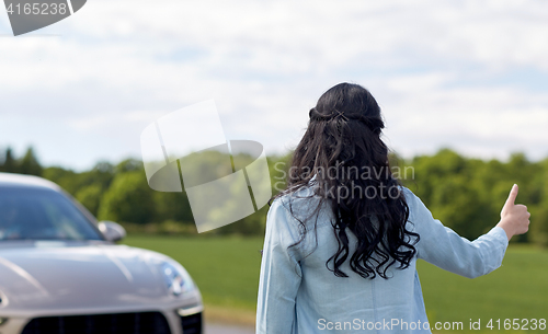 Image of woman hitchhiking and stopping car with thumbs up