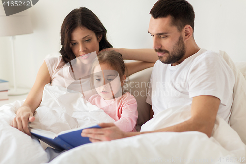 Image of happy family reading book in bed at home