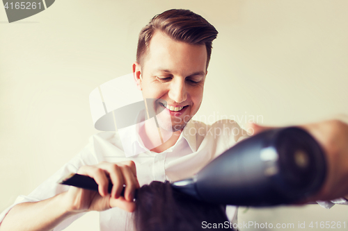 Image of happy stylist with fan making blow-dry at salon