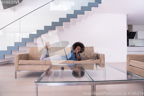 Image of African American woman using laptop on sofa