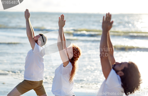 Image of group of people making yoga exercises on beach