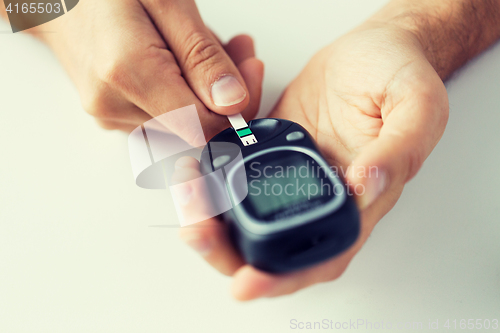 Image of close up of man checking blood sugar by glucometer