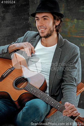 Image of Cool guy sitting with guitar on gray background