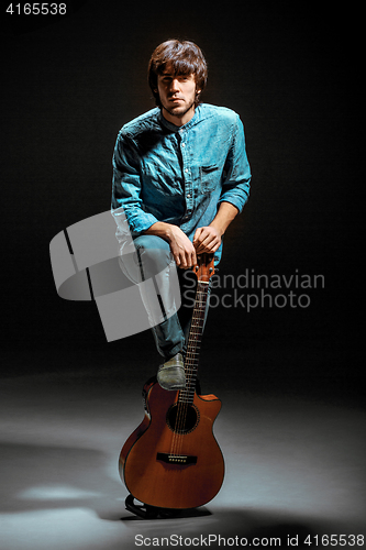 Image of Cool guy standing with guitar on dark background