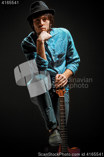 Image of Cool guy standing with guitar on dark background