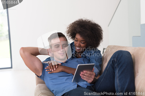 Image of multiethnic couple relaxing at  home with tablet computers