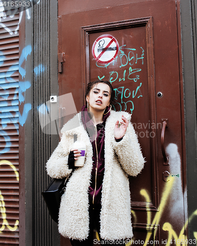 Image of young pretty stylish teenage girl outside at city wall with graf