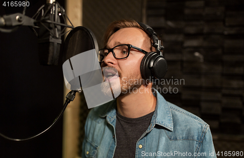 Image of man with headphones singing at recording studio