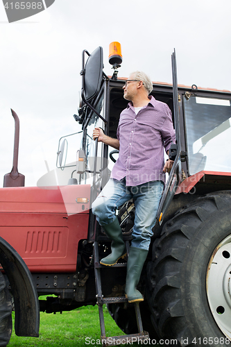 Image of old man or farmer getting out of tractor at farm