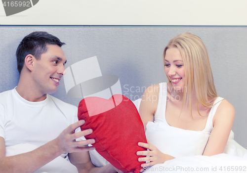 Image of smiling couple in bed with red heart shape pillow