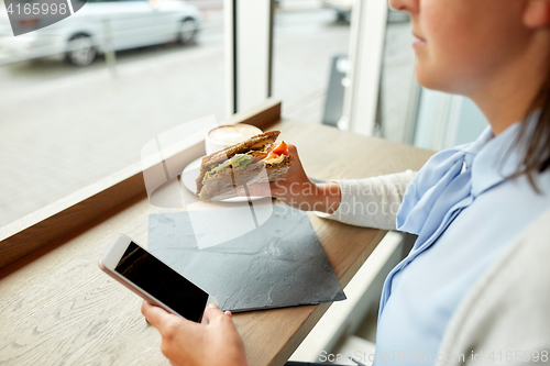 Image of woman with smartphone and sandwich at restaurant