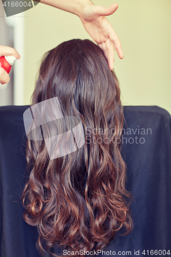 Image of stylist with hair spray making hairdo at salon