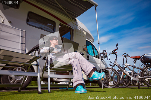 Image of Woman sitting on a chair near the camper and looking at a laptop