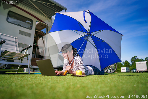 Image of Woman on the grass, looking at the laptop under umbrella near th