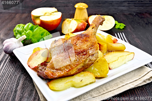 Image of Duck leg with apple and potatoes in plate on napkin