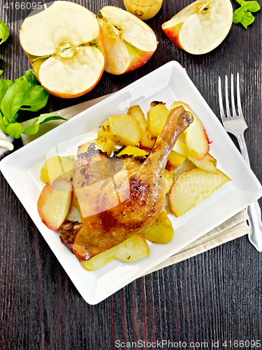 Image of Duck leg with apple and basil in plate on dark board top