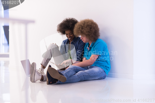 Image of multiethnic couple sitting on the floor with a laptop and tablet