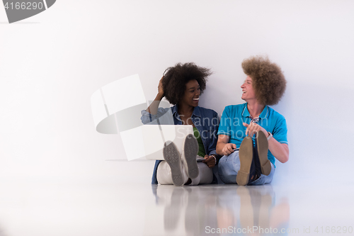 Image of multiethnic couple sitting on the floor with a laptop and tablet