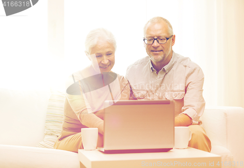 Image of happy senior couple with laptop and cups at home