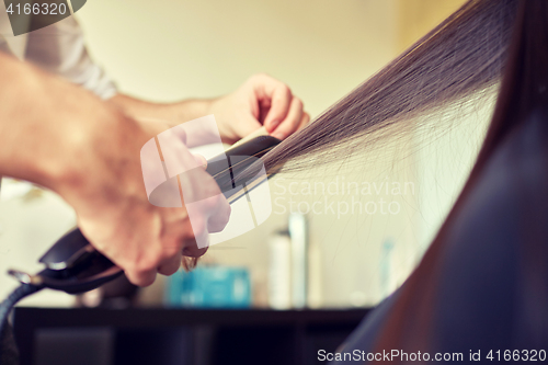 Image of stylist with iron straightening hair at salon