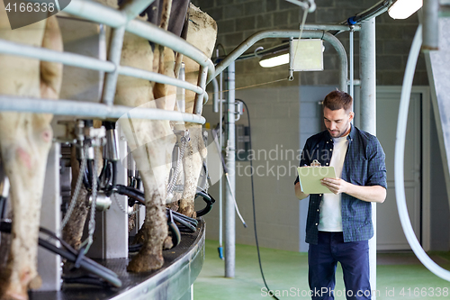 Image of man with clipboard and milking cows on dairy farm