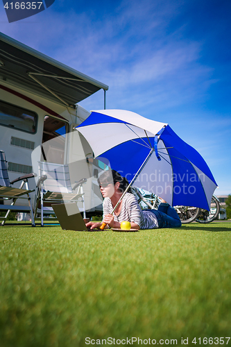 Image of Woman on the grass, looking at the laptop under umbrella near th