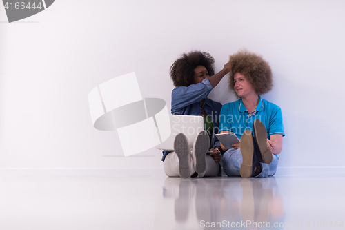 Image of multiethnic couple sitting on the floor with a laptop and tablet