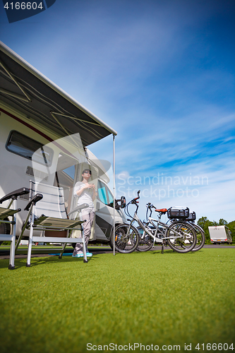 Image of Woman is standing with a mug of coffee near the camper.