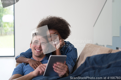 Image of multiethnic couple relaxing at  home with tablet computers